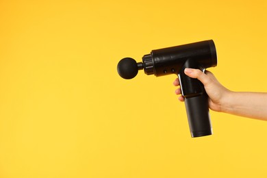 Woman holding percussive massager on yellow background, closeup. Space for text