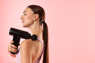 Woman using percussive massager to relieve trapezius muscle on pink background. Space for text