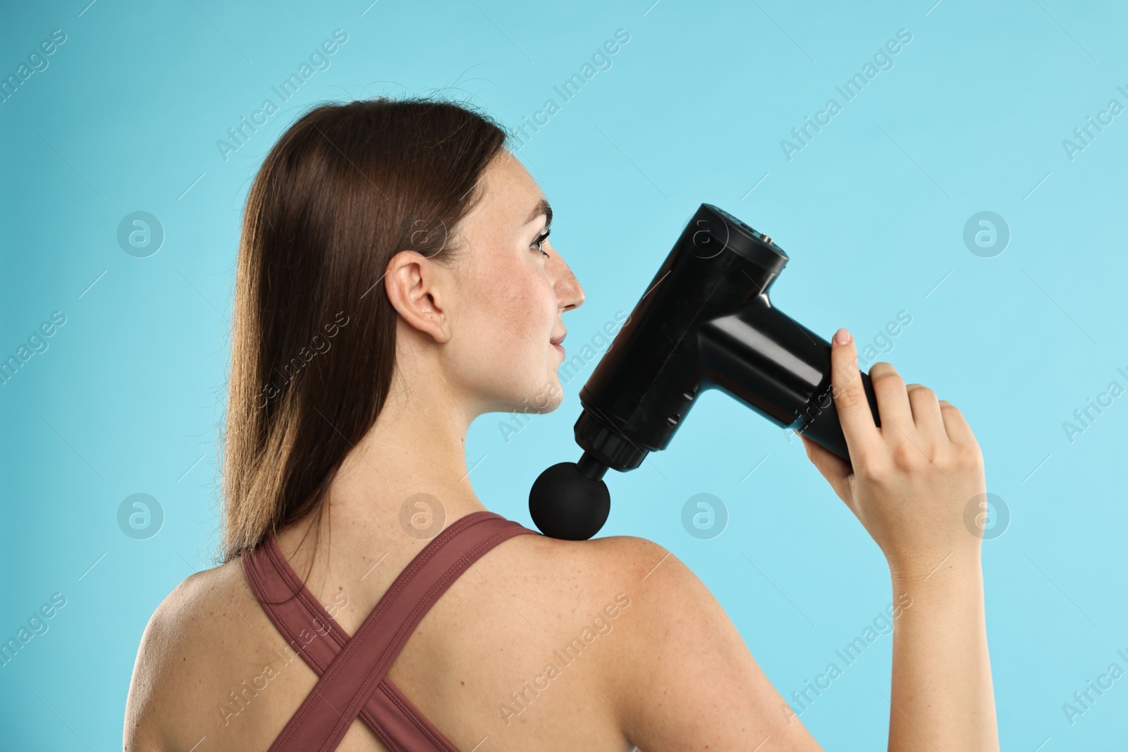 Photo of Woman using percussive massager to relieve trapezius muscle on light blue background, back view