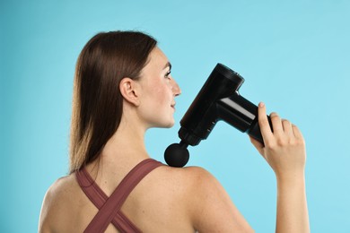 Woman using percussive massager to relieve trapezius muscle on light blue background, back view