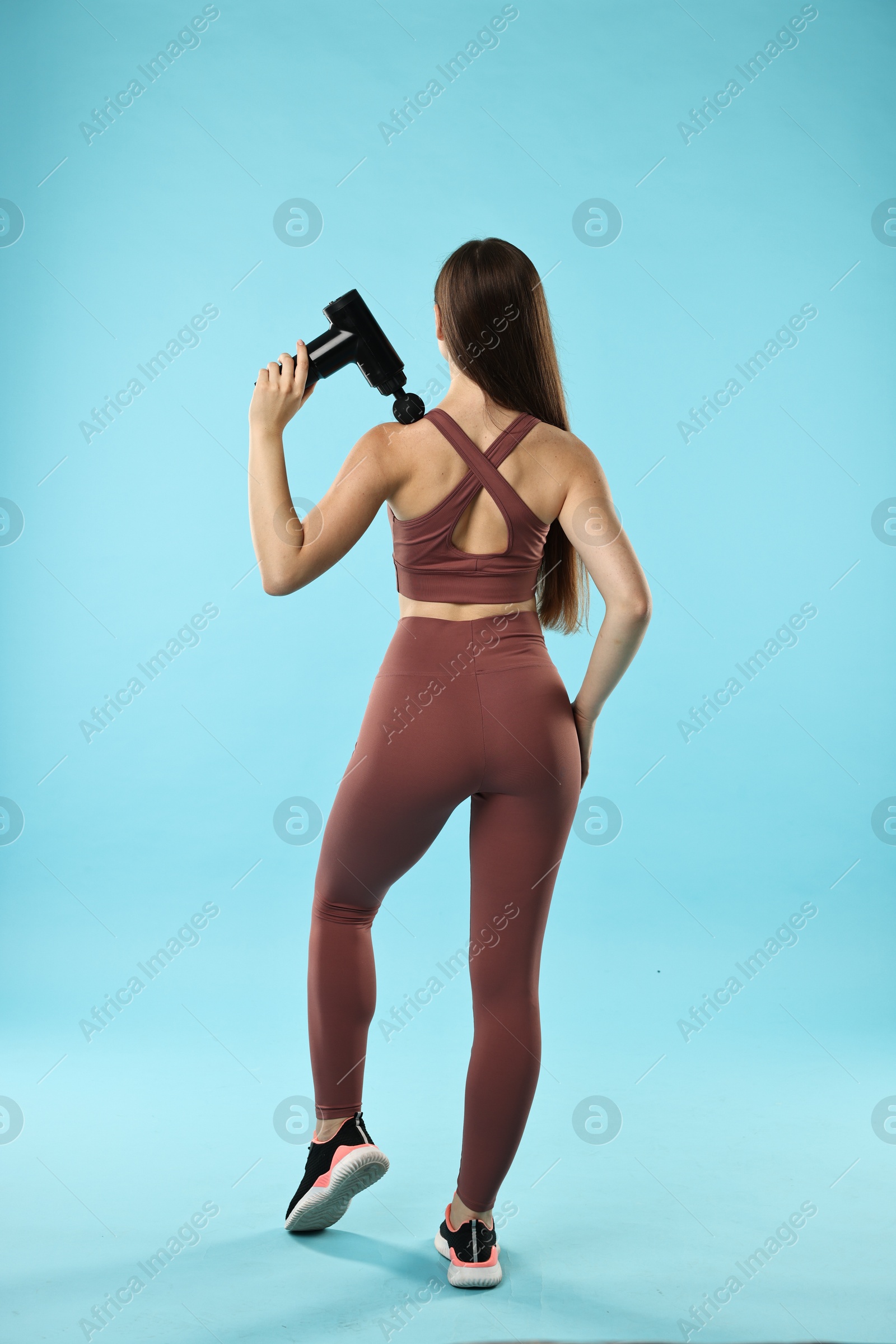 Photo of Woman using percussive massager to relieve trapezius muscle on light blue background, back view