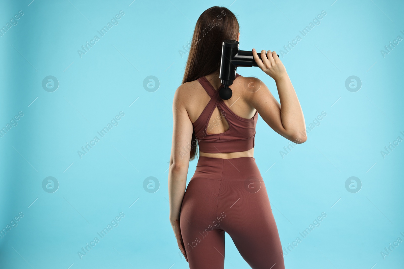 Photo of Woman using percussive massager to relieve back muscles on light blue background, back view