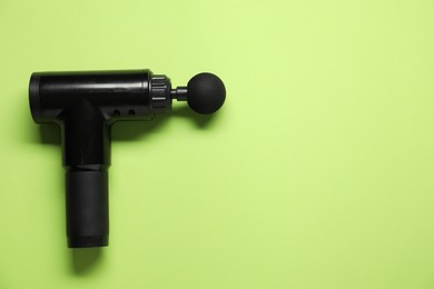 One black percussive massager on green background, top view. Space for text