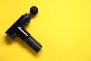 Photo of One black percussive massager on yellow background, top view. Space for text