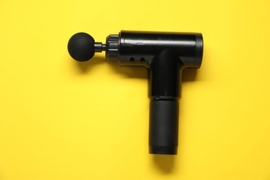 Photo of One black percussive massager on yellow background, top view