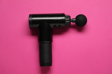 One black percussive massager on pink background, top view