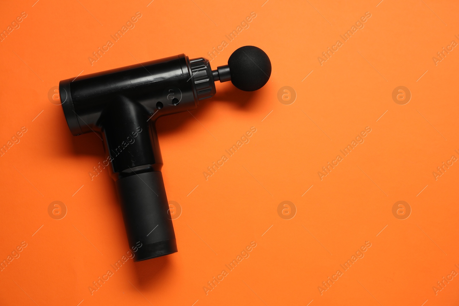 Photo of One black percussive massager on orange background, top view. Space for text