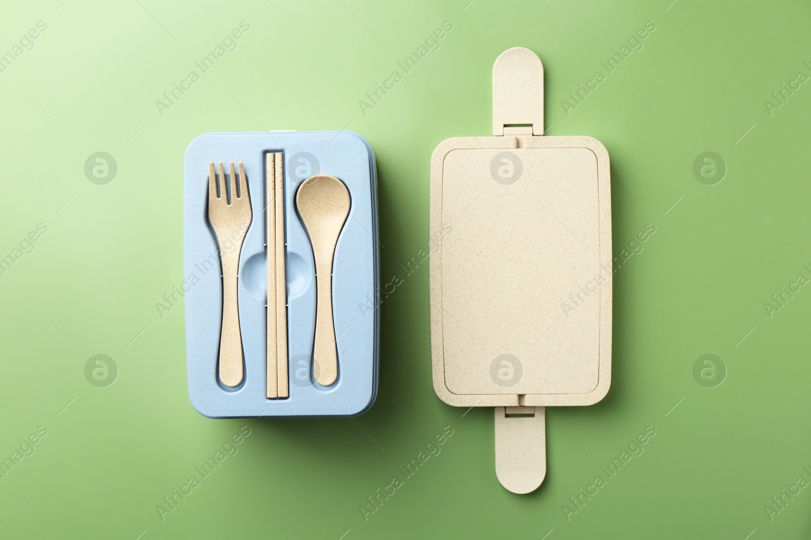 Photo of Plastic lunch box with cutlery and lid on green background, top view