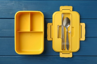 Photo of Yellow lunch box with cutlery on blue wooden table, top view