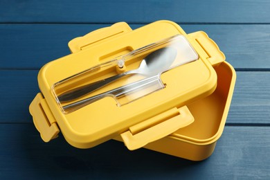 Photo of Yellow lunch box with cutlery on blue wooden table