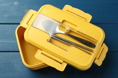 Photo of Yellow lunch box with cutlery on blue wooden table, above view