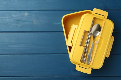 Photo of Yellow lunch box with cutlery on blue wooden table, top view. Space for text