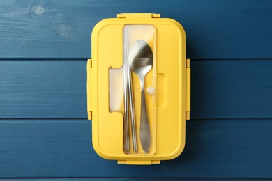 Photo of Yellow lunch box with cutlery on blue wooden table, top view