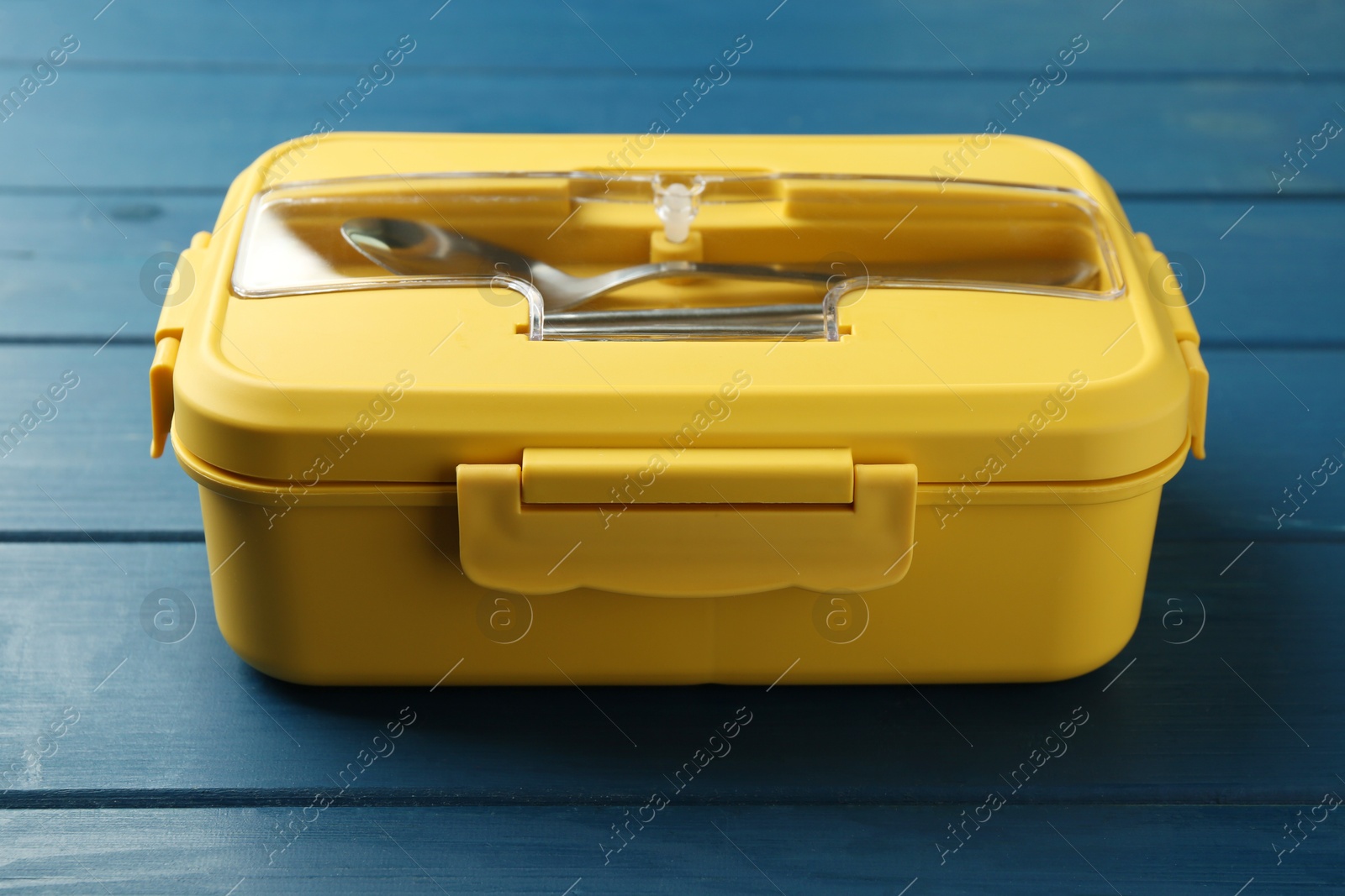 Photo of Yellow lunch box with cutlery on blue wooden table, closeup