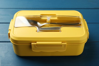 Photo of Yellow lunch box with cutlery on blue wooden table, closeup