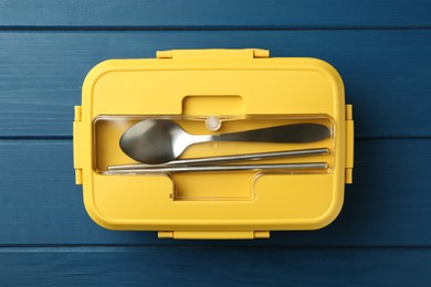 Photo of Yellow lunch box with cutlery on blue wooden table, top view