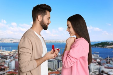 Man with engagement ring making marriage proposal to his girlfriend. Couple against cityscape