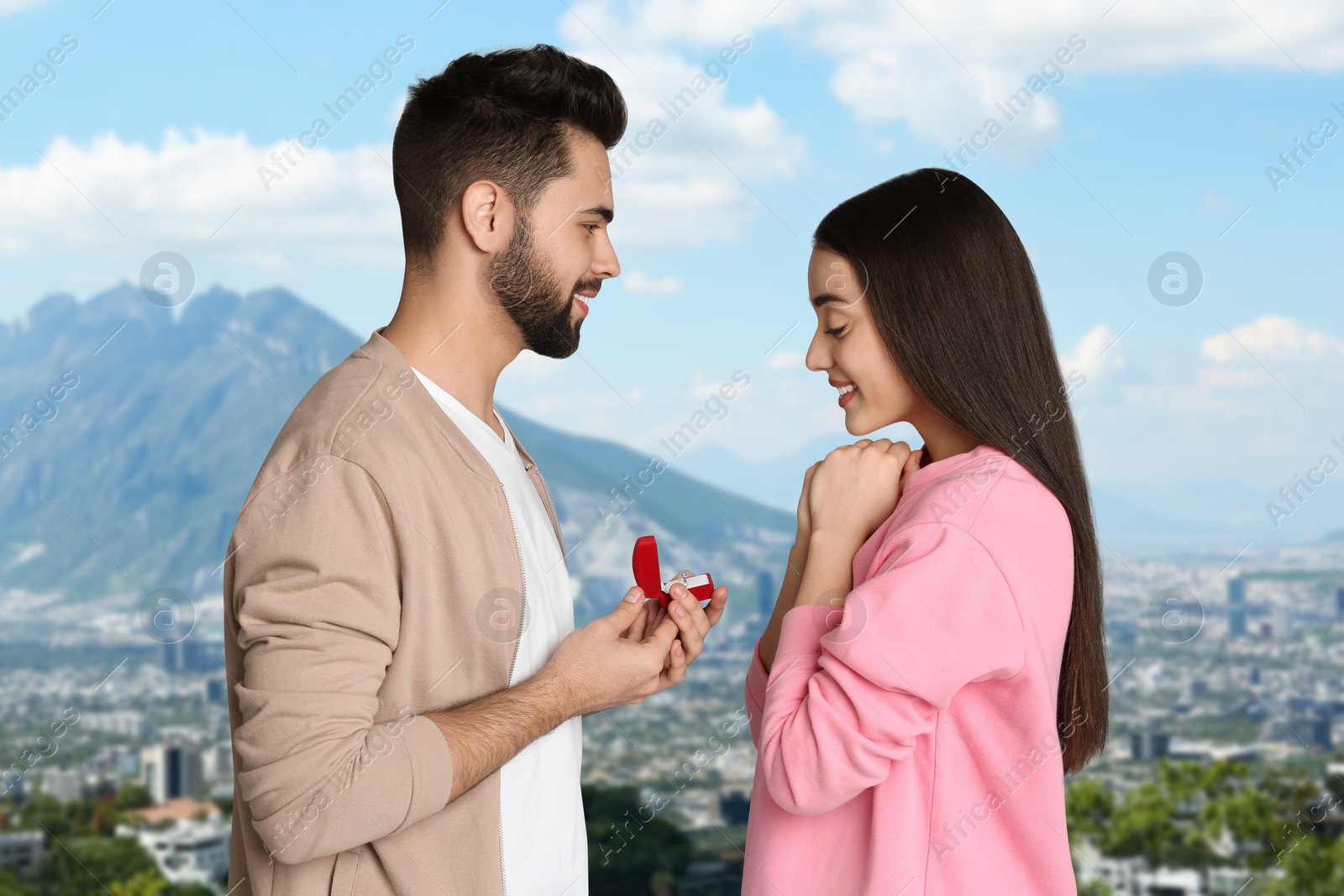 Image of Man with engagement ring making marriage proposal to his girlfriend. Couple against cityscape