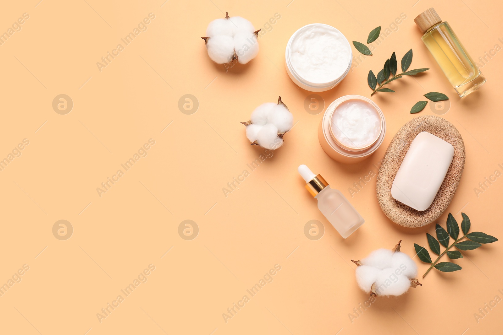 Photo of Different cosmetic products, leaves and cotton flowers on pale orange background, flat lay. Space for text