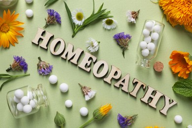 Photo of Word Homeopathy, pills and medicinal herbs on olive background, flat lay