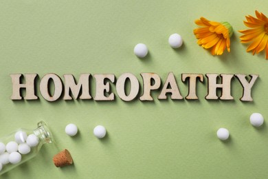 Photo of Word Homeopathy, pills and medicinal herbs on olive background, flat lay