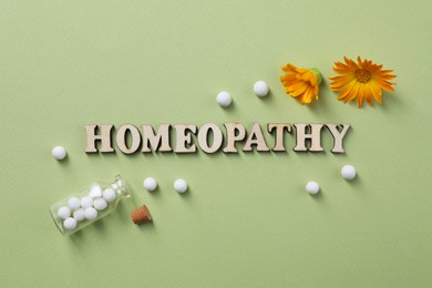 Photo of Word Homeopathy, pills and medicinal herbs on olive background, flat lay