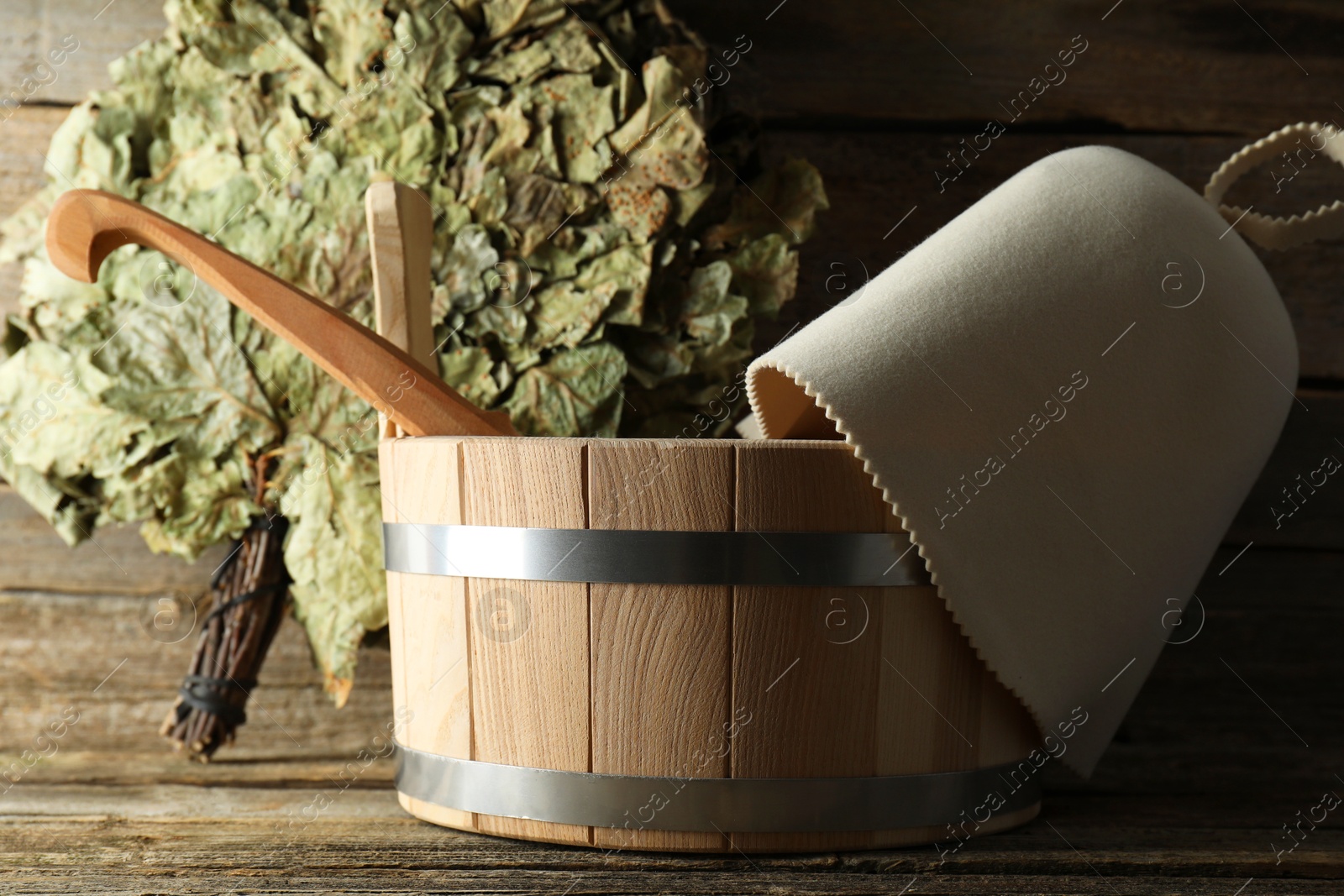 Photo of Sauna equipment. Bucket with ladle, felt wool hat and oak whisk on wooden surface