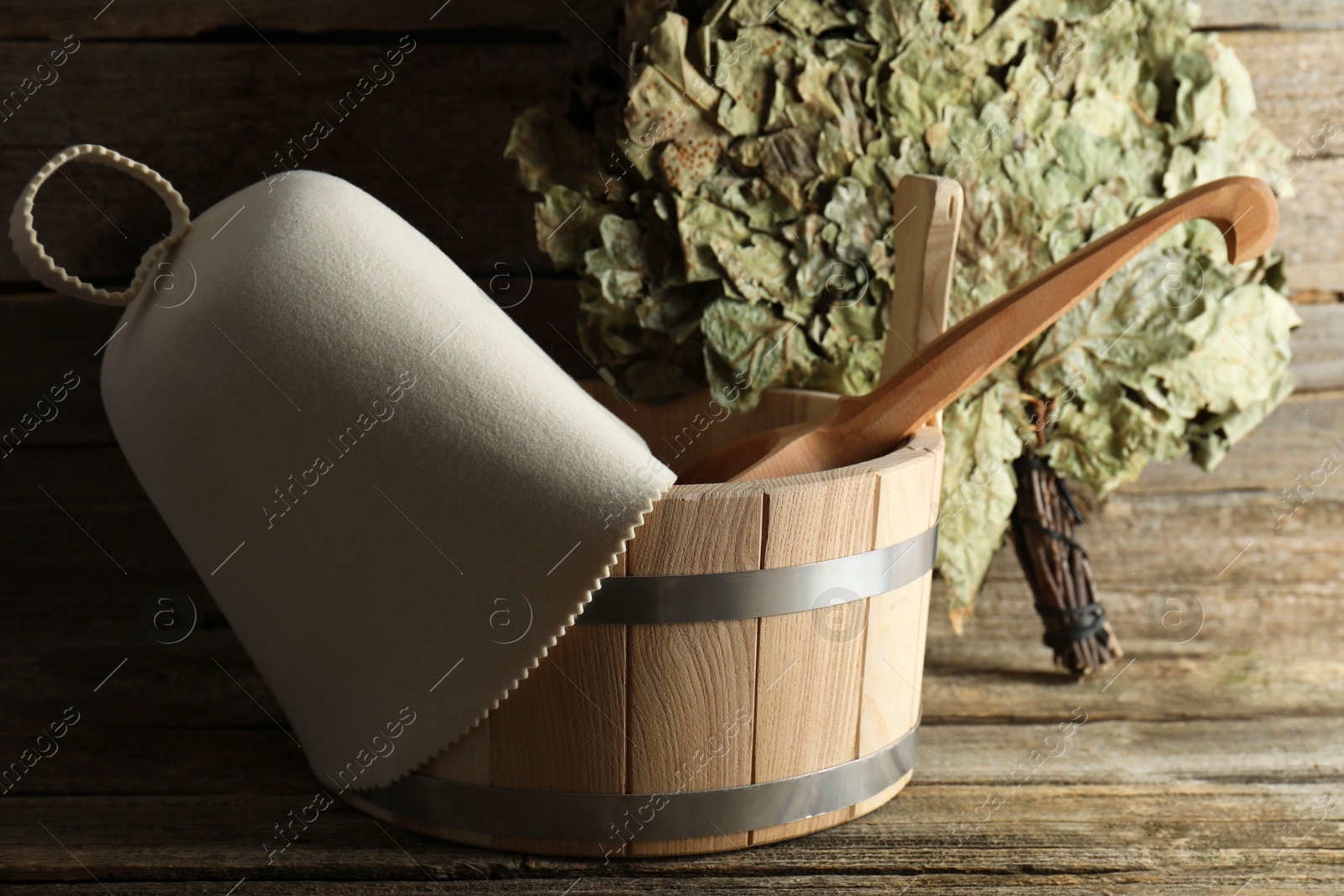 Photo of Sauna equipment. Bucket with ladle, felt wool hat and oak whisk on wooden surface