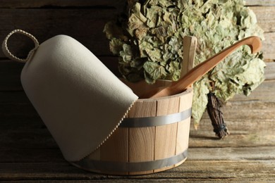 Photo of Sauna equipment. Bucket with ladle, felt wool hat and oak whisk on wooden surface