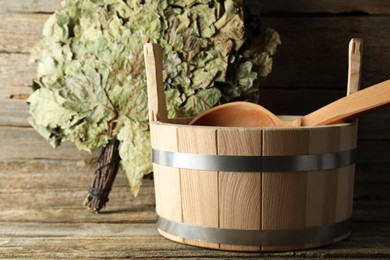 Sauna equipment. Bucket with ladle and oak whisk on wooden surface