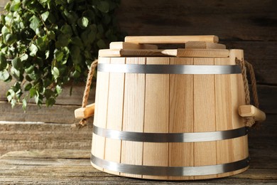 Photo of Sauna equipment. Bucket on wooden surface and birch whisk indoors