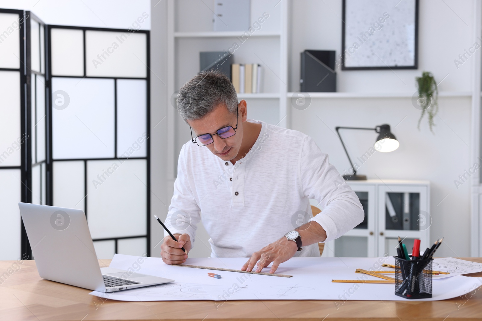 Photo of Architect making engineering drawing at wooden table in office