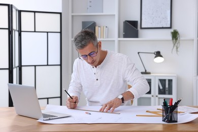 Photo of Architect making engineering drawing at wooden table in office