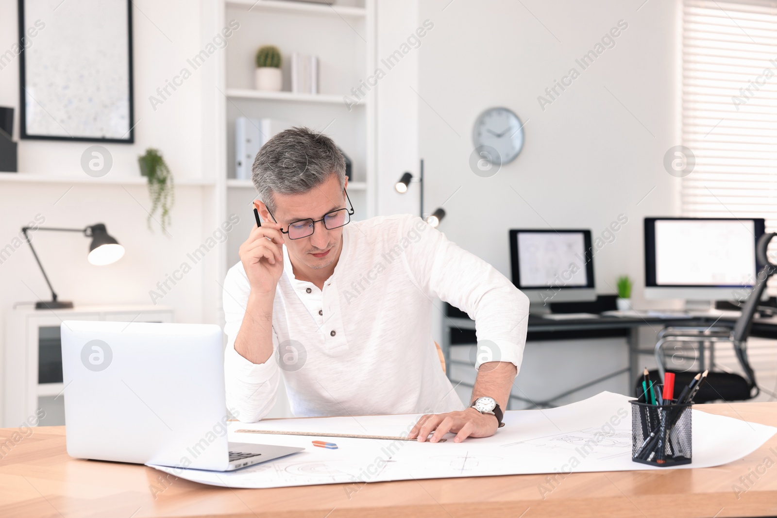 Photo of Architect making engineering drawing at wooden table in office