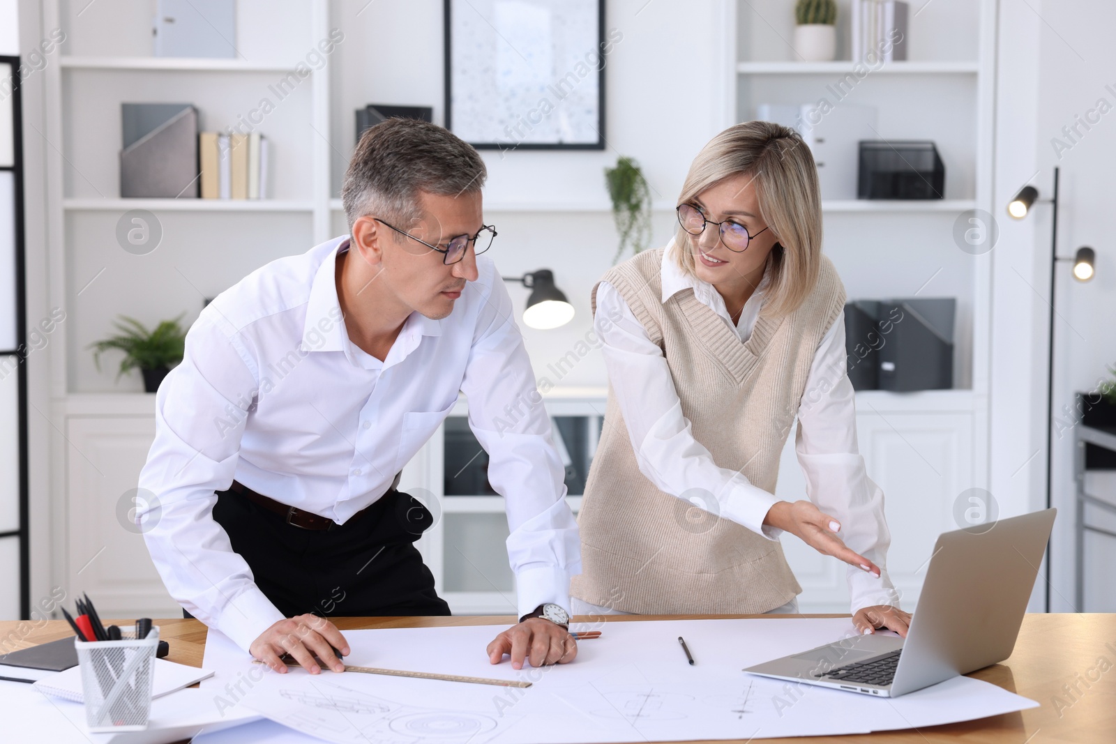 Photo of Architects discussing engineering drawing at wooden table in office