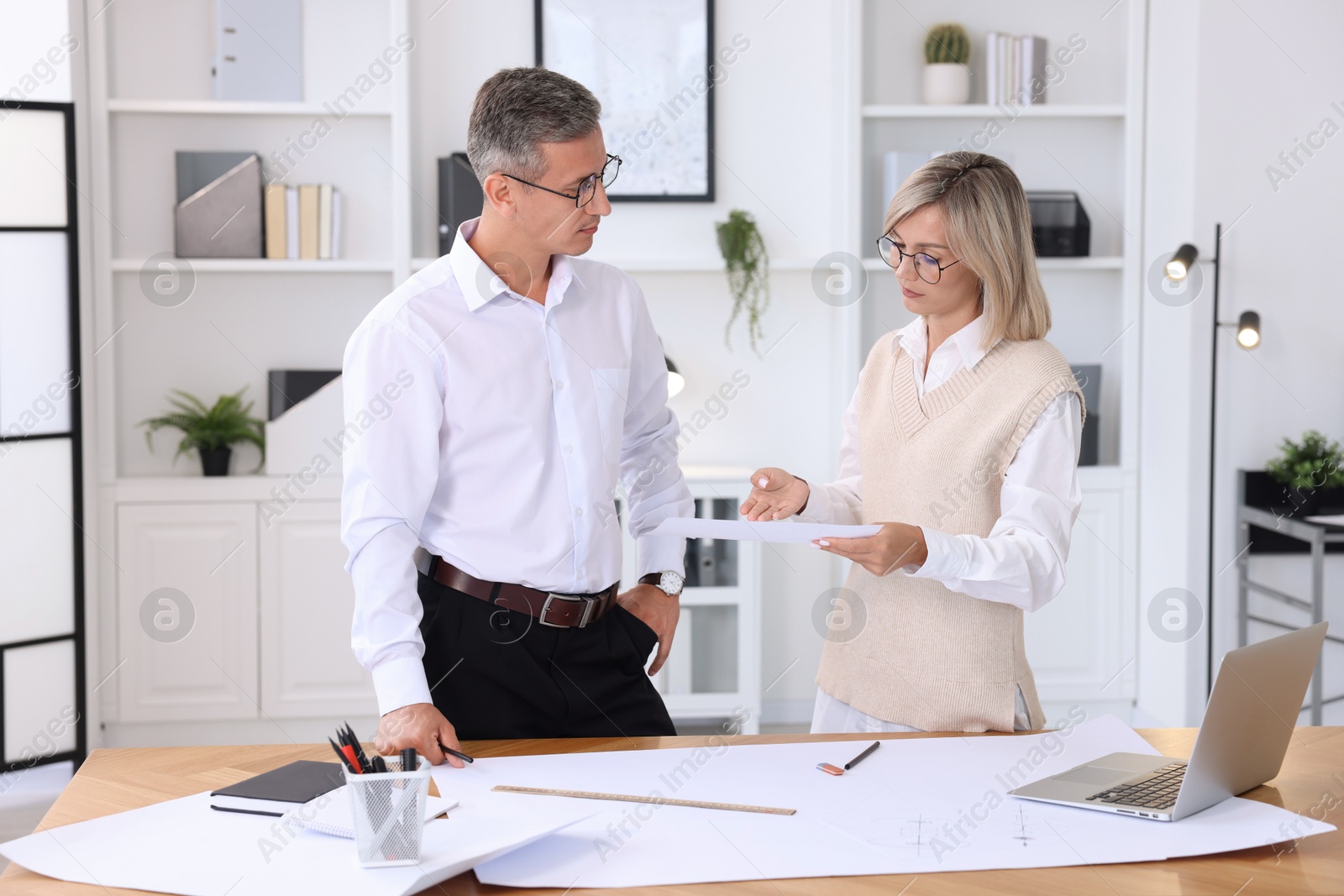 Photo of Architects discussing engineering drawing at wooden table in office