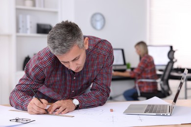 Architect making engineering drawing at table in office