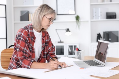 Architect making engineering drawing at table in office