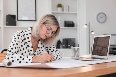 Architect making engineering drawing at wooden table in office