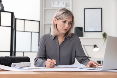 Architect making engineering drawing at wooden table in office