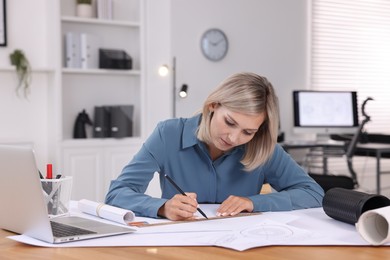 Architect making engineering drawing at table in office