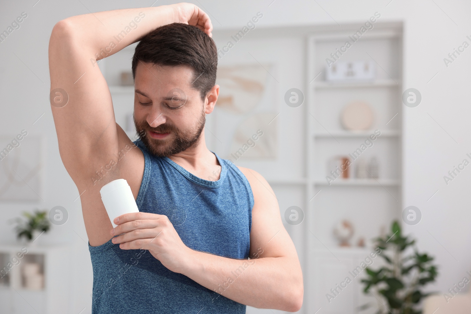 Photo of Handsome man applying solid deodorant at home. Space for text