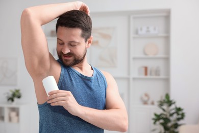 Handsome man applying solid deodorant at home. Space for text