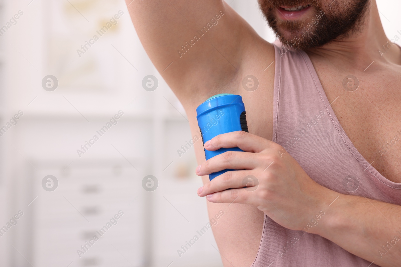 Photo of Man applying solid deodorant at home, closeup. Space for text