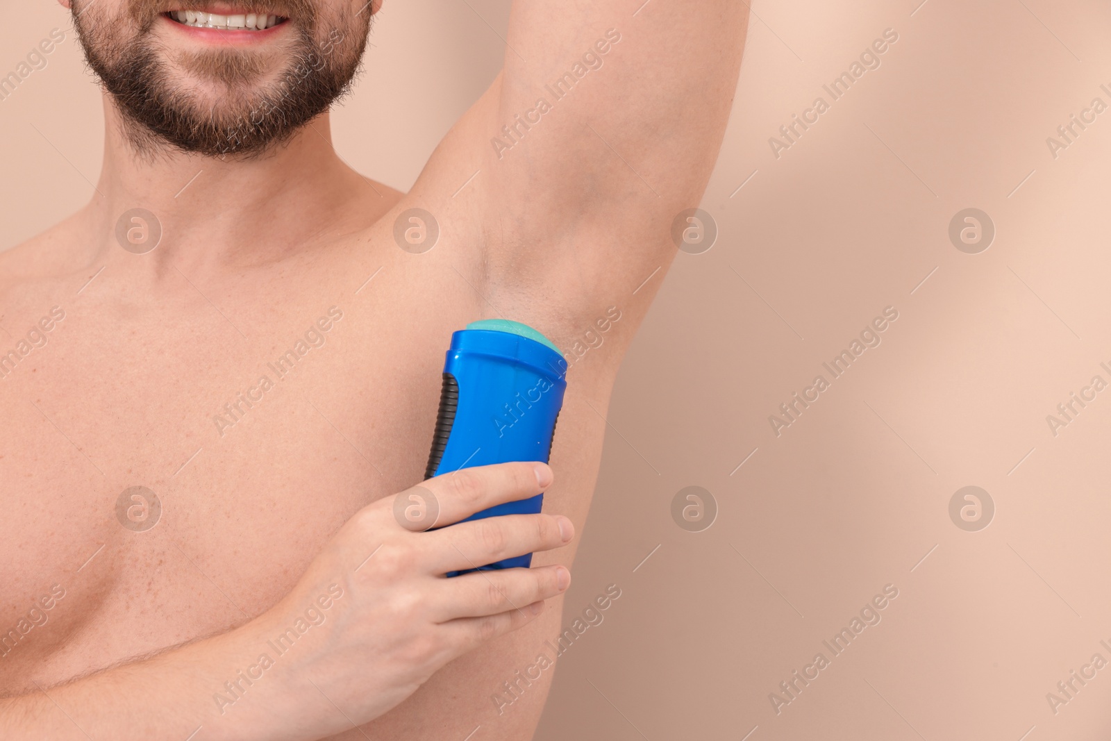 Photo of Smiling man applying solid deodorant on beige background, closeup. Space for text