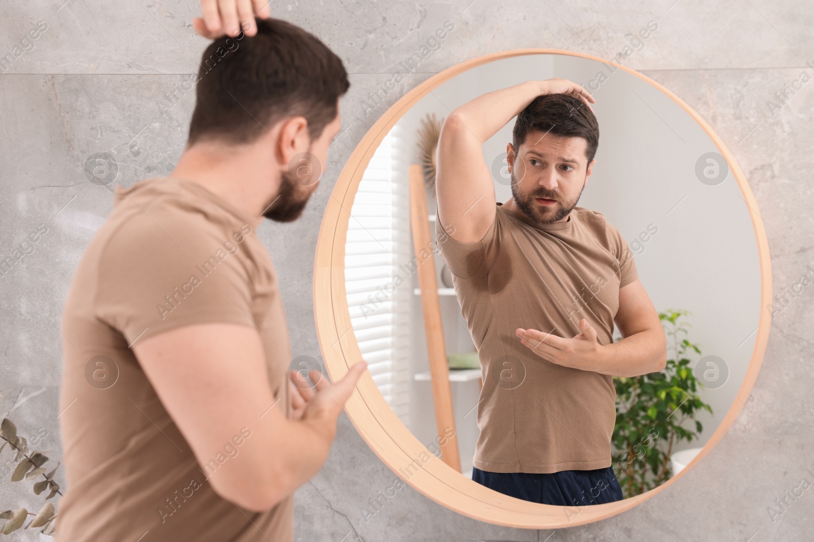 Photo of Emotional man in t-shirt before using deodorant near mirror at home