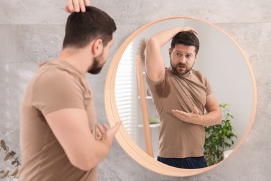 Photo of Emotional man in t-shirt before using deodorant near mirror at home