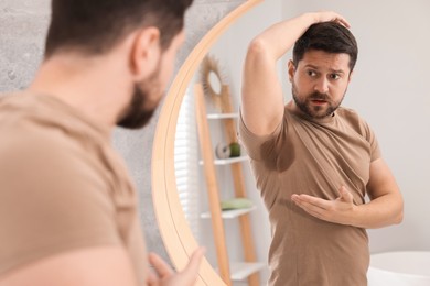 Emotional man in t-shirt before using deodorant near mirror at home