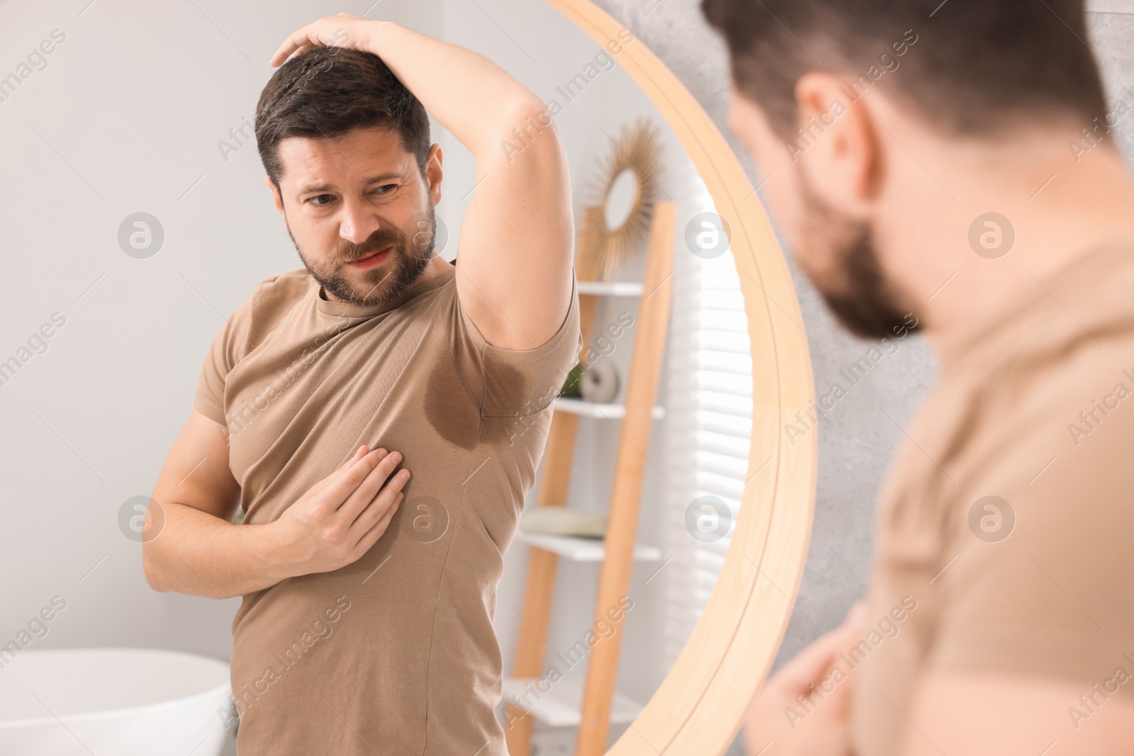 Photo of Emotional man in t-shirt before using deodorant near mirror at home