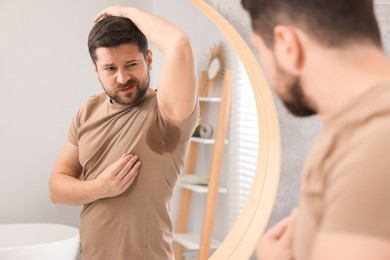 Emotional man in t-shirt before using deodorant near mirror at home